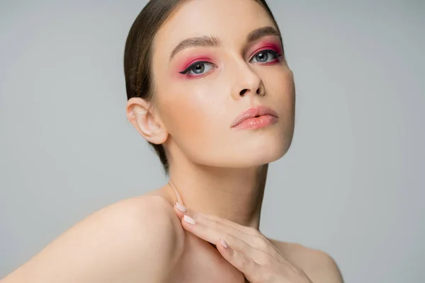 Young woman with perfect skin and makeup touching bare shoulder and looking at camera isolated on grey — Stock Photo