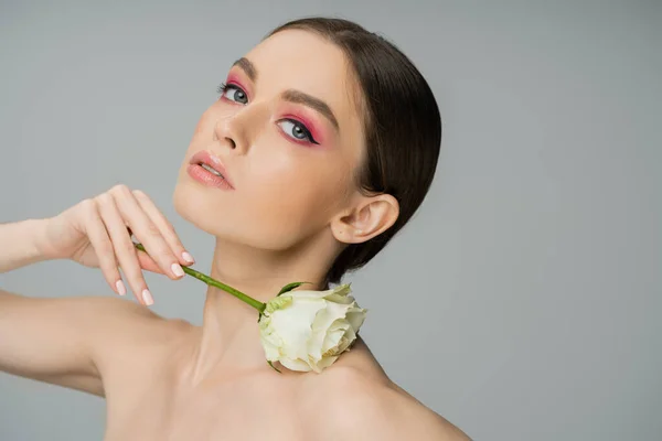 Sensual woman with makeup and naked shoulder posing with ivory rose isolated on grey - foto de stock