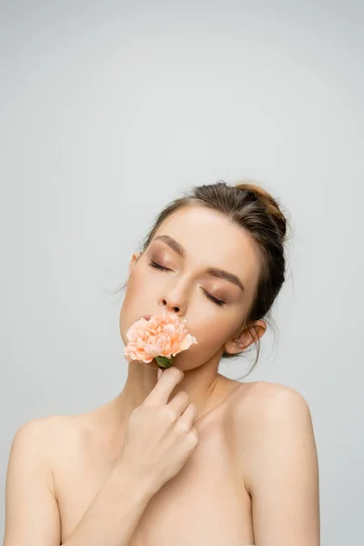 Young woman with closed eyes and makeup smelling aromatic carnation isolated on grey — Stock Photo