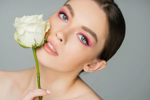 Портрет очаровательной женщины, позирующей с белой розой рядом идеальное лицо изолированы на сером — стоковое фото
