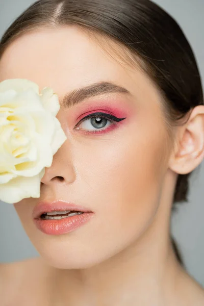 Close up portrait of young woman with pink visage obscuring face with ivory rose isolated on grey — Stock Photo