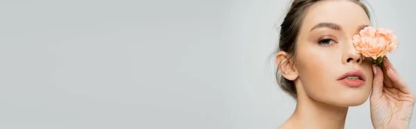 Ritratto di giovane donna con pelle perfetta che copre l'occhio con garofano fresco isolato su grigio, striscione — Foto stock