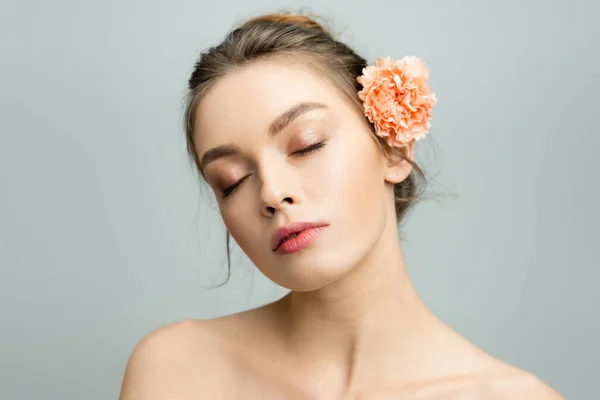 Portrait of charming woman with closed eyes and fresh carnation flower behind ear isolated on grey — Stock Photo