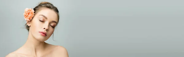 Charming woman with naked shoulders and carnation flower in hair posing with closed eyes isolated on grey, banner — Stock Photo