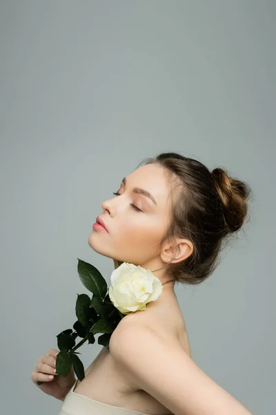 Sensual woman with closed eyes holding fresh rose near naked shoulder isolated on grey — Stock Photo