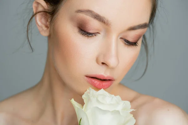 Donna affascinante con pelle pulita e trucco naturale guardando rosa bianca isolata sul grigio — Foto stock