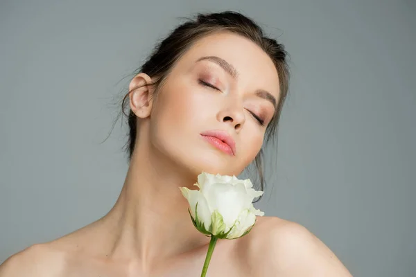 Young woman with natural makeup and naked shoulders posing with closed eyes near white rose isolated on grey — Foto stock