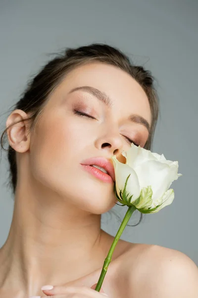 Charming woman with natural makeup and closed eyes posing with white rose near face isolated on grey — Stock Photo