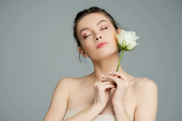 Giovane donna con le spalle nude e gli occhi chiusi tenendo rosa bianca isolata su grigio — Foto stock