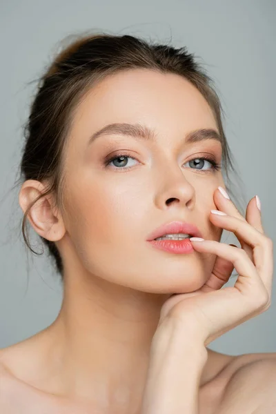 Young and pretty woman with natural makeup posing with hand near face isolated on grey — Stock Photo