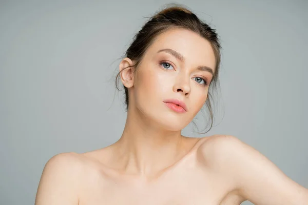 Charming woman with natural makeup and naked shoulders looking at camera isolated on grey - foto de stock