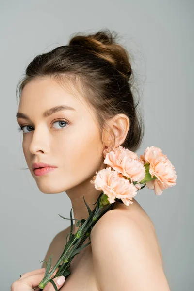 Young fair haired woman with naked shoulders holding carnations isolated on grey — Stock Photo