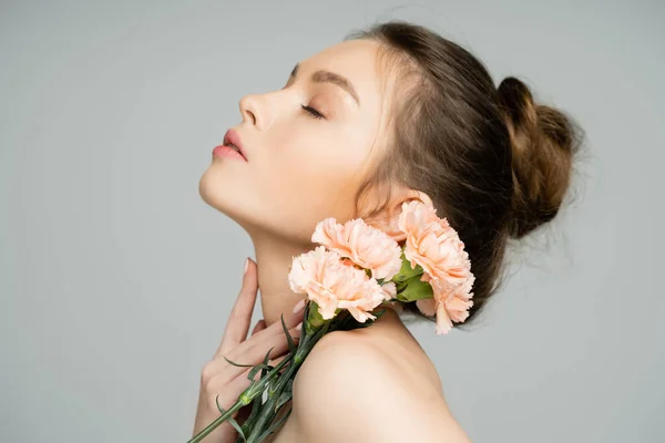 Young woman with carnations touching neck isolated on grey — Stock Photo