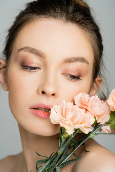 Portrait of woman with natural makeup posing with carnations isolated on grey - foto de stock