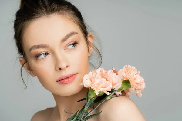 Bella donna dai capelli biondi guardando lontano vicino garofani isolati su grigio — Foto stock