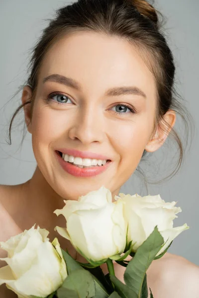 Portrait of cheerful young woman looking at camera near rose flowers isolated on grey — Stock Photo