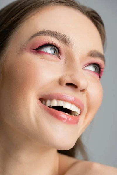 Smiling young woman with pink eye shadow looking away isolated on grey — Stock Photo