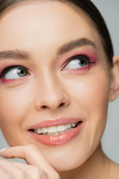Close up view of smiling woman with pink eye shadows looking away isolated on grey — Stock Photo