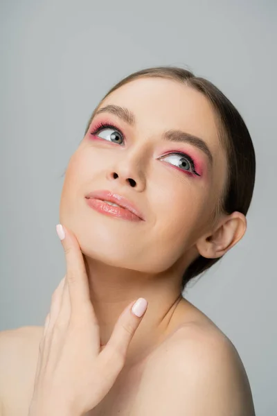 Portrait of joyful woman with pink eye shadow touching face isolated on grey — Stock Photo