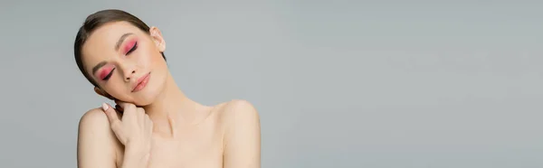 Young woman with bright makeup touching naked shoulder isolated on grey, banner — Stock Photo