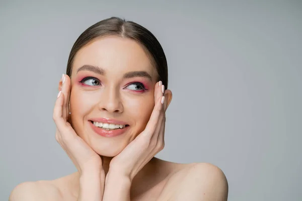 Smiling woman with bright visage and naked shoulders touching cheeks isolated on grey — Stock Photo