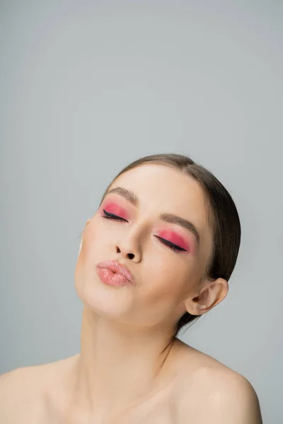 Mujer joven con maquillaje brillante pucheros labios aislados en gris — Stock Photo