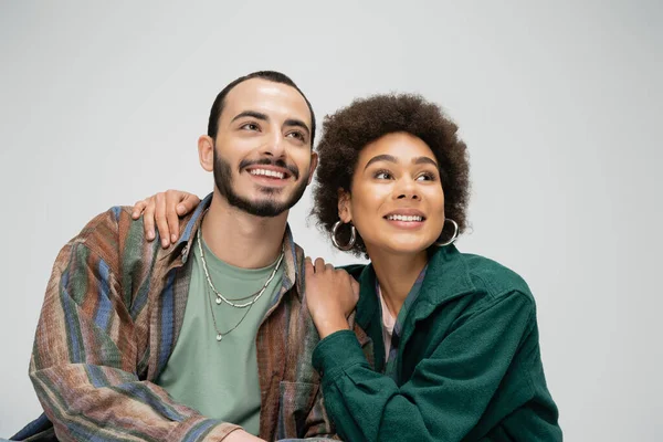 Happy african american woman hugging shoulders of bearded man while looking away isolated on grey — Stockfoto