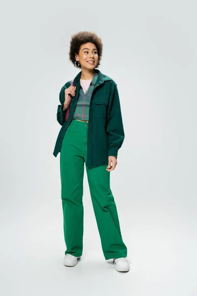 Full length of young african american woman in stylish outfit smiling and looking away on grey background — Stock Photo