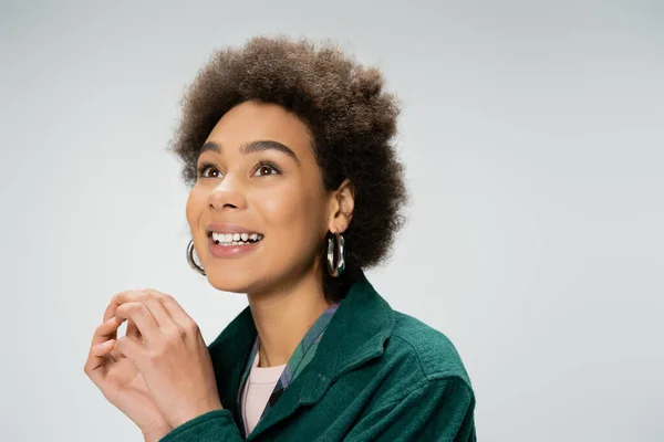 Portrait of excited african american woman with curly brunette hair and hoop earrings looking away isolated on grey — Stock Photo