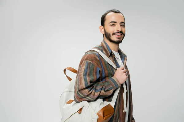 Lächelnder bärtiger Student in buntem Hemd steht mit Rucksack isoliert auf grau — Stockfoto