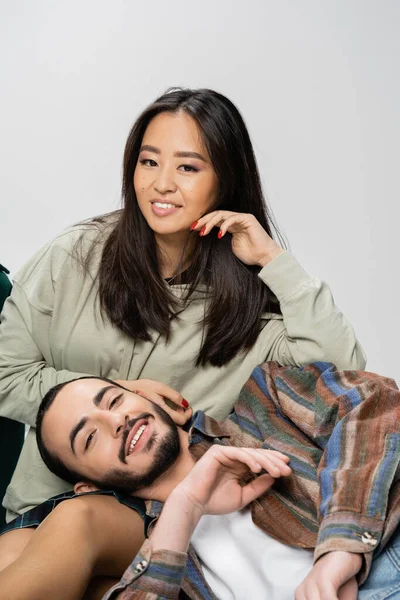 Glückliches gemischtrassiges Paar in trendigen Klamotten, das isoliert auf grau in die Kamera lächelt — Stockfoto