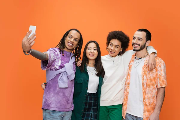 Cheerful man with dreadlocks taking selfie with young multicultural friends isolated on orange — Foto stock