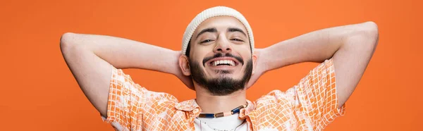 Portrait of happy bearded man with hands behind head looking at camera isolated on orange, banner — Stockfoto