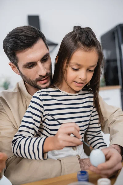 Child coloring Easer egg near bearded father in kitchen — Stock Photo