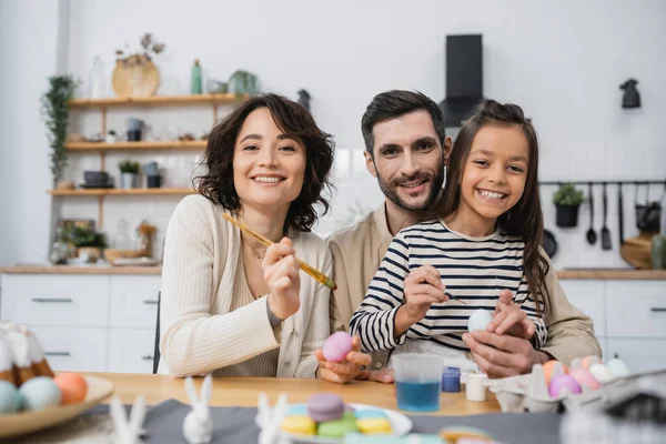 Smiling family looking at camera while coloring Easer eggs in kitchen — Stock Photo