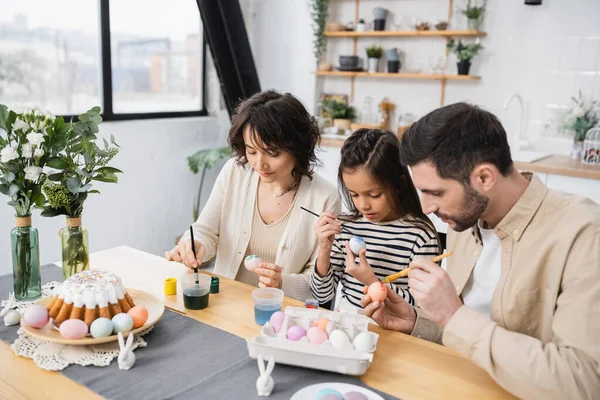 Family coloring Easter eggs near tasty cake on table at home — Stock Photo