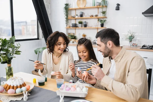 Smiling parents and child coloring eggs near Easter cake at home — Stock Photo