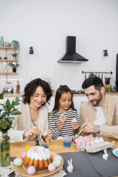 Smiling daughter and parents coloring Easter eggs in kitchen — Photo de stock