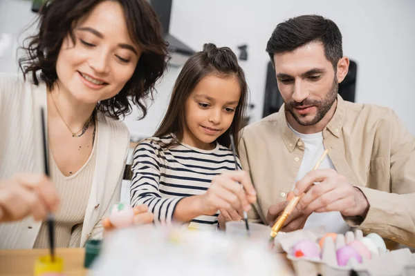 Kid holding paintbrush while coloring Easter eggs with parents in kitchen — Stock Photo