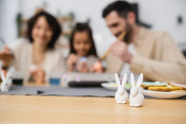 Easter rabbits near blurred parents and child in kitchen — Stock Photo