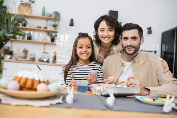 Família sorrindo olhando para a câmera enquanto colore ovos Easer na cozinha — Fotografia de Stock