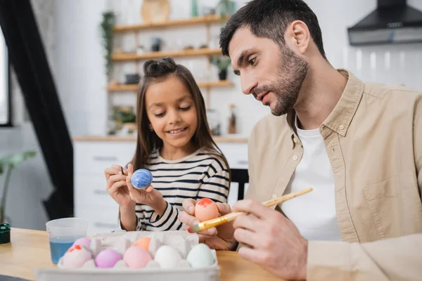 Father and happy daughter coloring Easter eggs in kitchen — Stock Photo