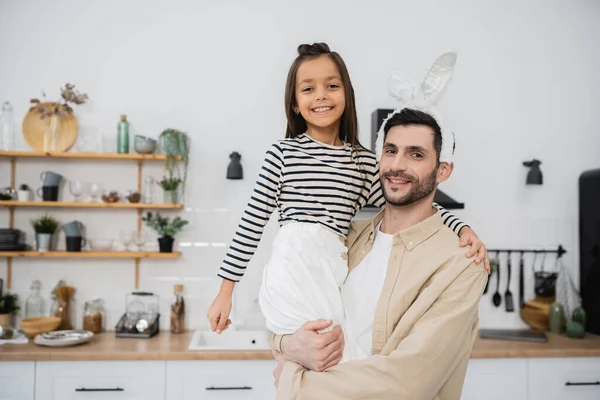 Smiling man with Easter headband holding daughter at home — Stock Photo