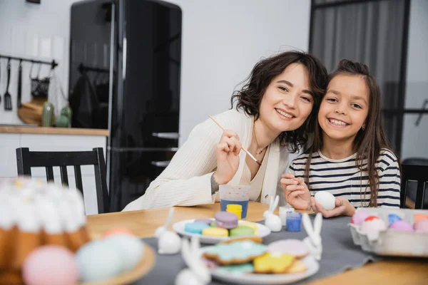 Mother and daughter looking at camera while coloring Easter eggs at home — Stock Photo