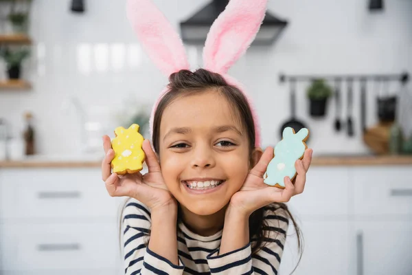 Smiling kid in Easter headband with bunny ears holding cookies in kitchen — Fotografia de Stock