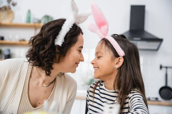 Vista lateral de mãe sorridente e filha em headbands de Páscoa em casa — Fotografia de Stock