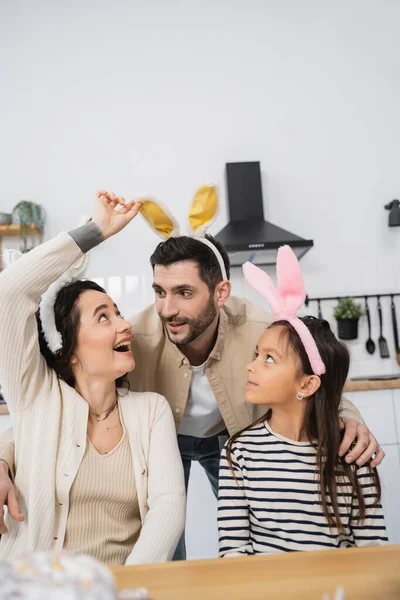 Smiling woman looking at Easter headband on husband near daughter at home — Stock Photo