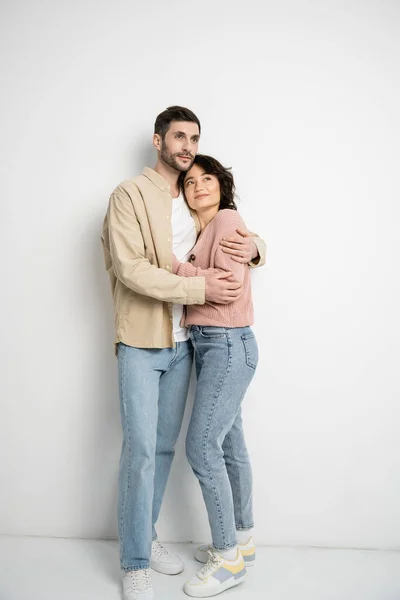 Comprimento total do casal abraçando e olhando para longe no fundo branco — Fotografia de Stock