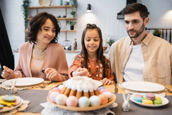 Criança sorridente tomando ovo de Páscoa durante o jantar com os pais em casa — Fotografia de Stock