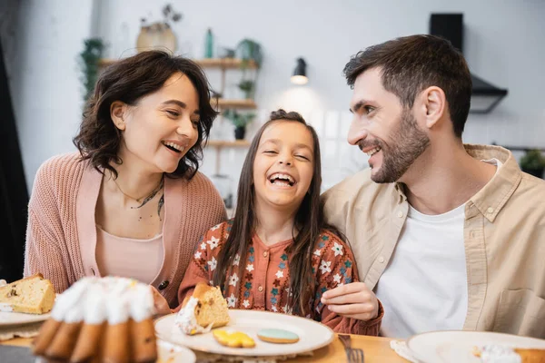 Cheerful girl sitting near parents during Easter dinner at home — Stock Photo